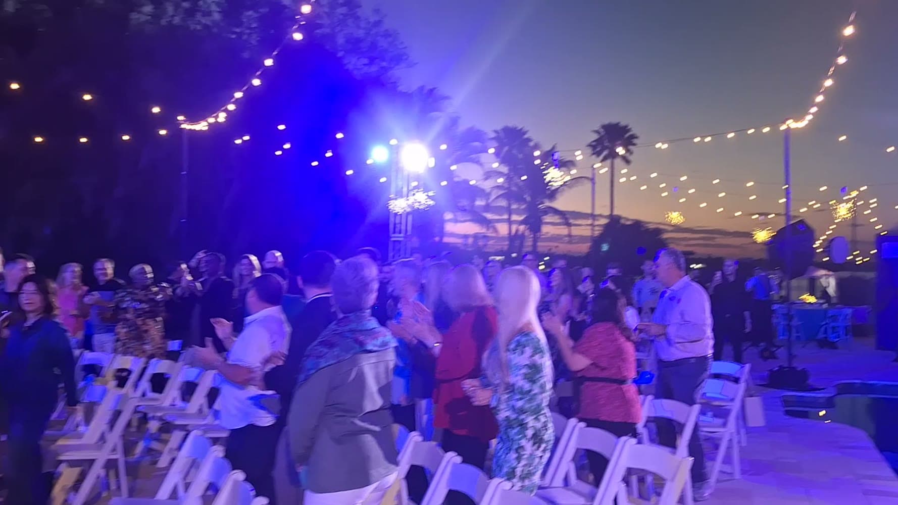 An outdoor evening event under string lights, the crowd on its feet at dusk