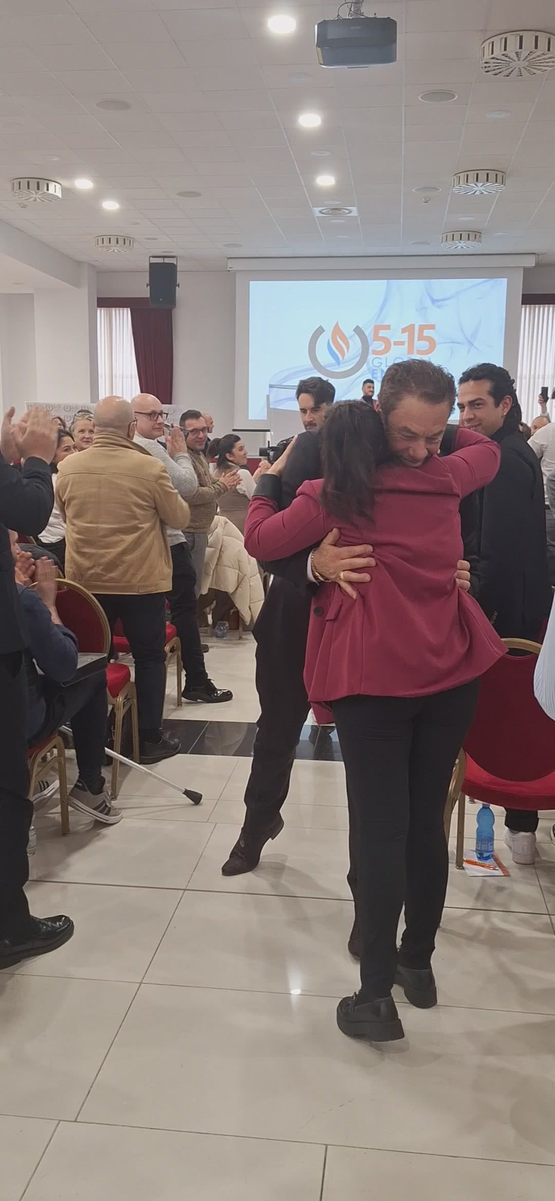 Tom lifting an attendee in a joyful embrace in the middle of a packed seminar hall in Bologna