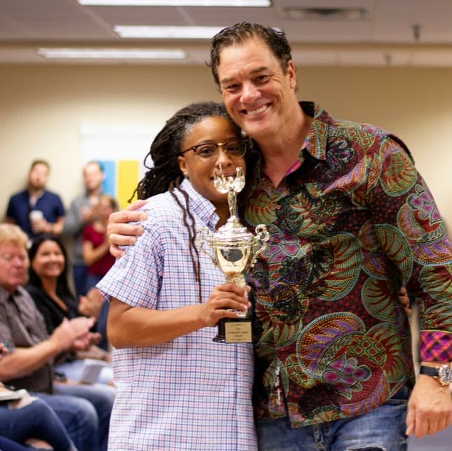 Tom Cummins embracing an employee holding a trophy at a company awards celebration