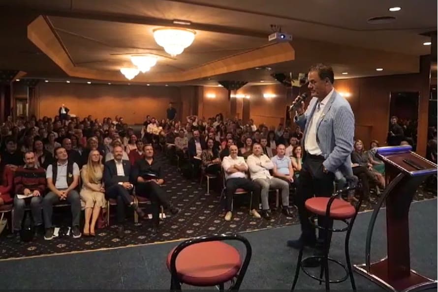 Tom Cummins addressing a full ballroom audience with a microphone